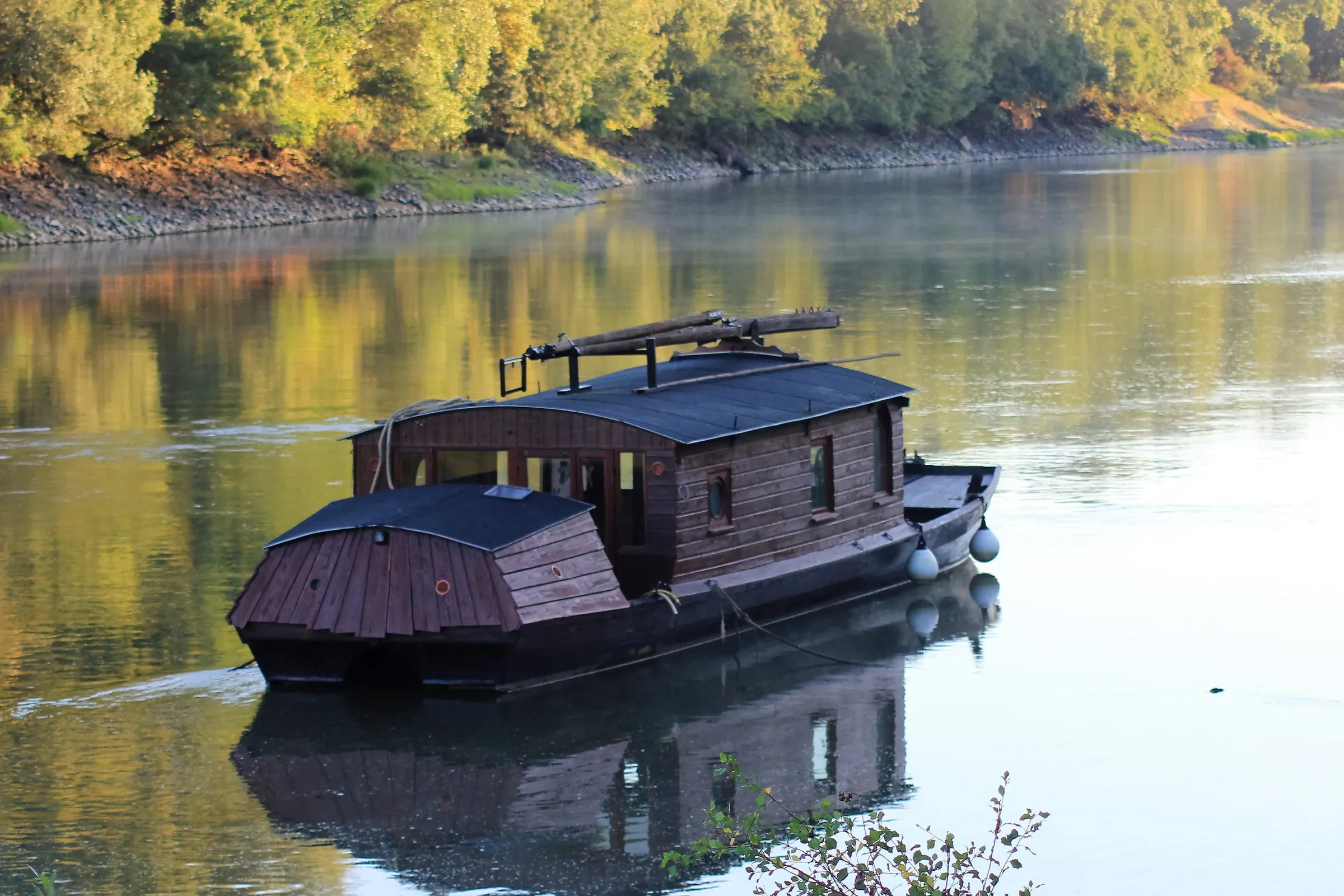 Cabin toue sailing on the Loire, golden reflections of trees on the water