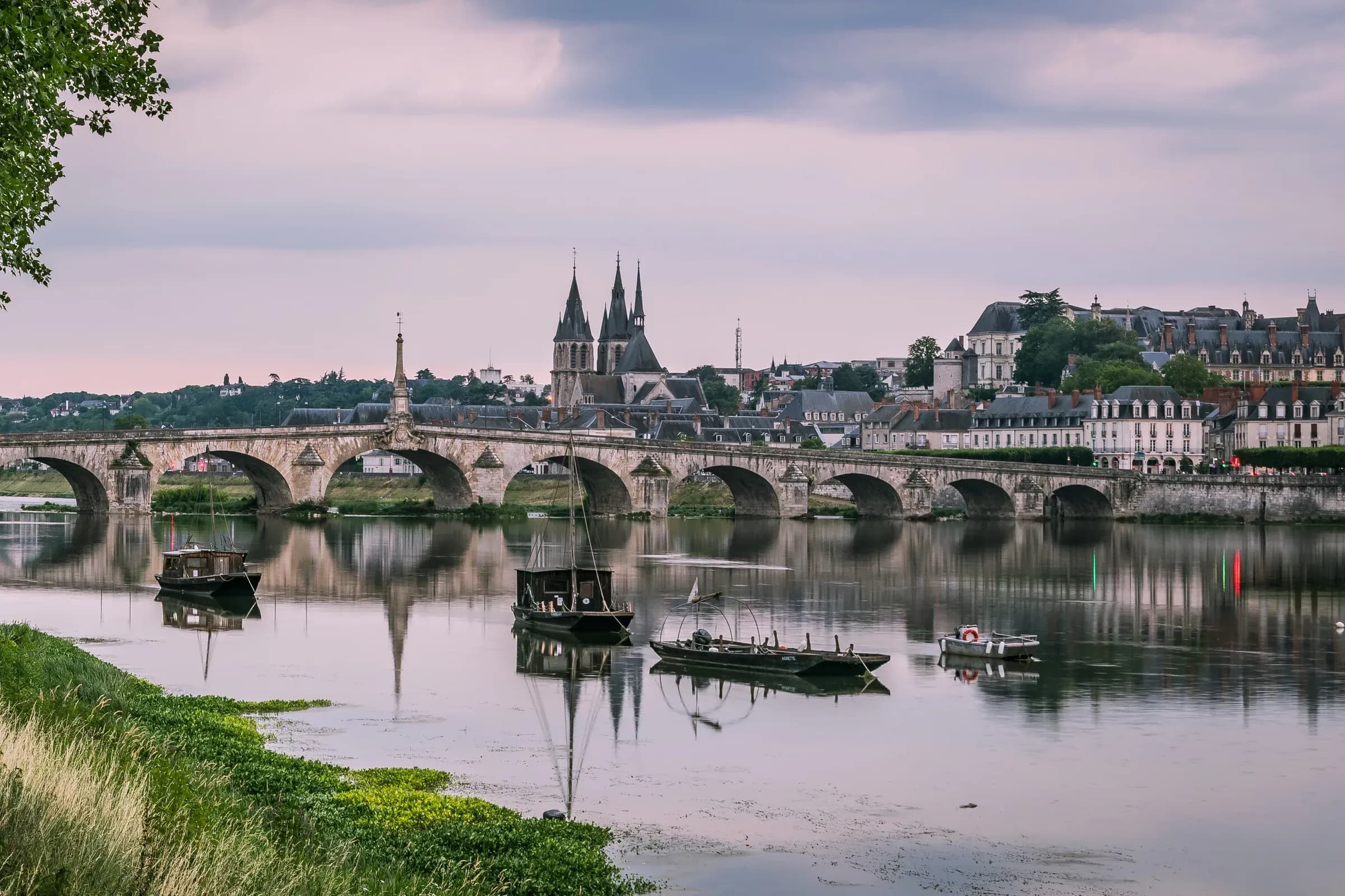 Blois au crépuscule : le pont Jacques-Gabriel, l'église Saint-Nicolas et le château royal reflétés dans la Loire