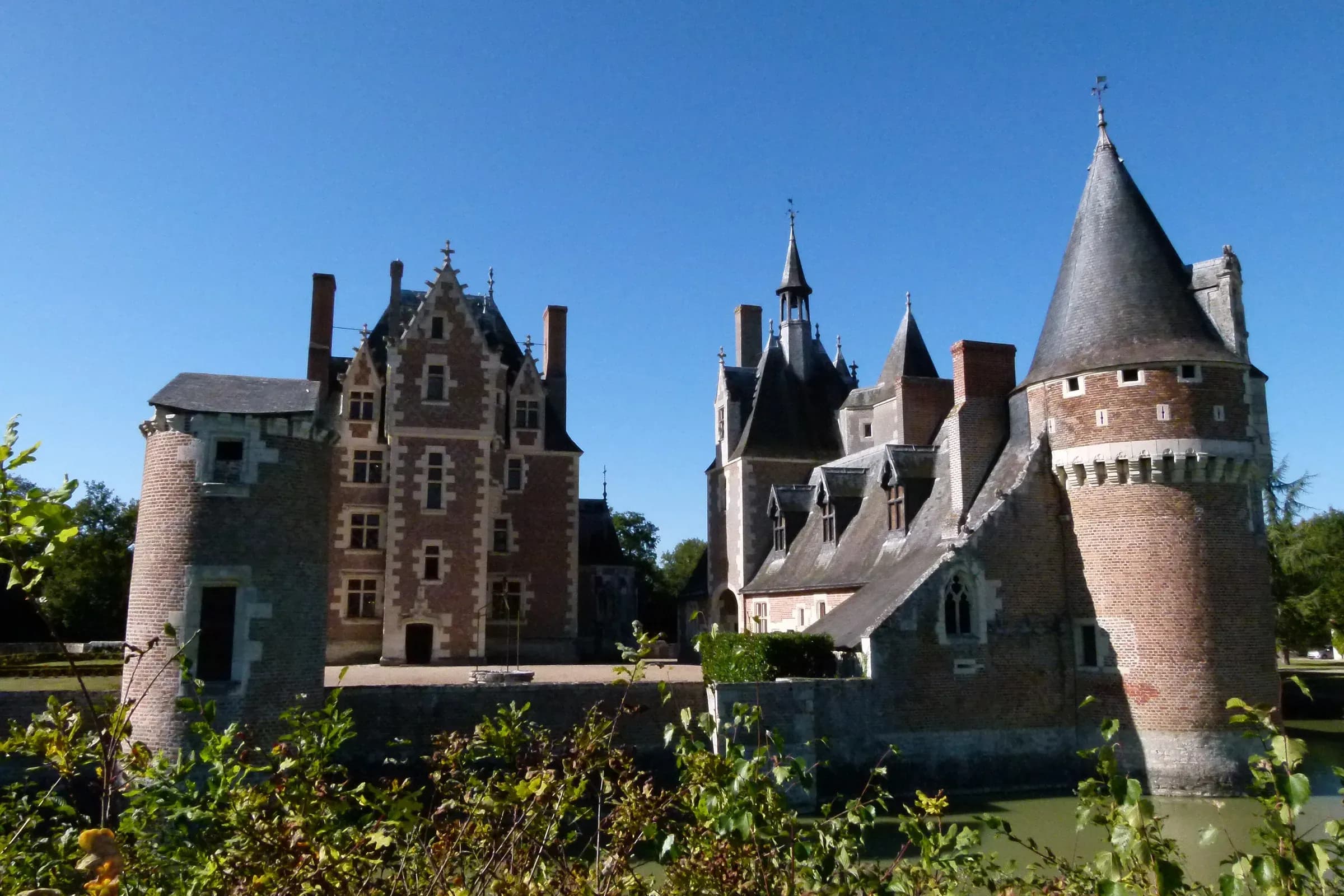 Le château du Moulin à Lassay-sur-Croisne, tours de brique rouge et toits d'ardoise sous un ciel bleu