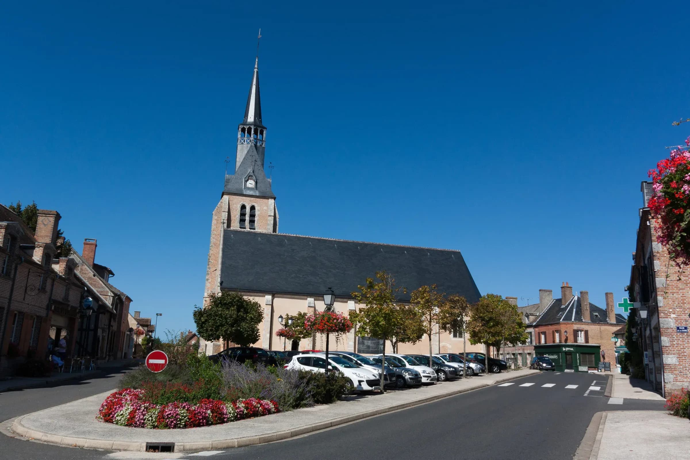 Church and flowered square of Chaumont-sur-Tharonne, ringed by brick houses