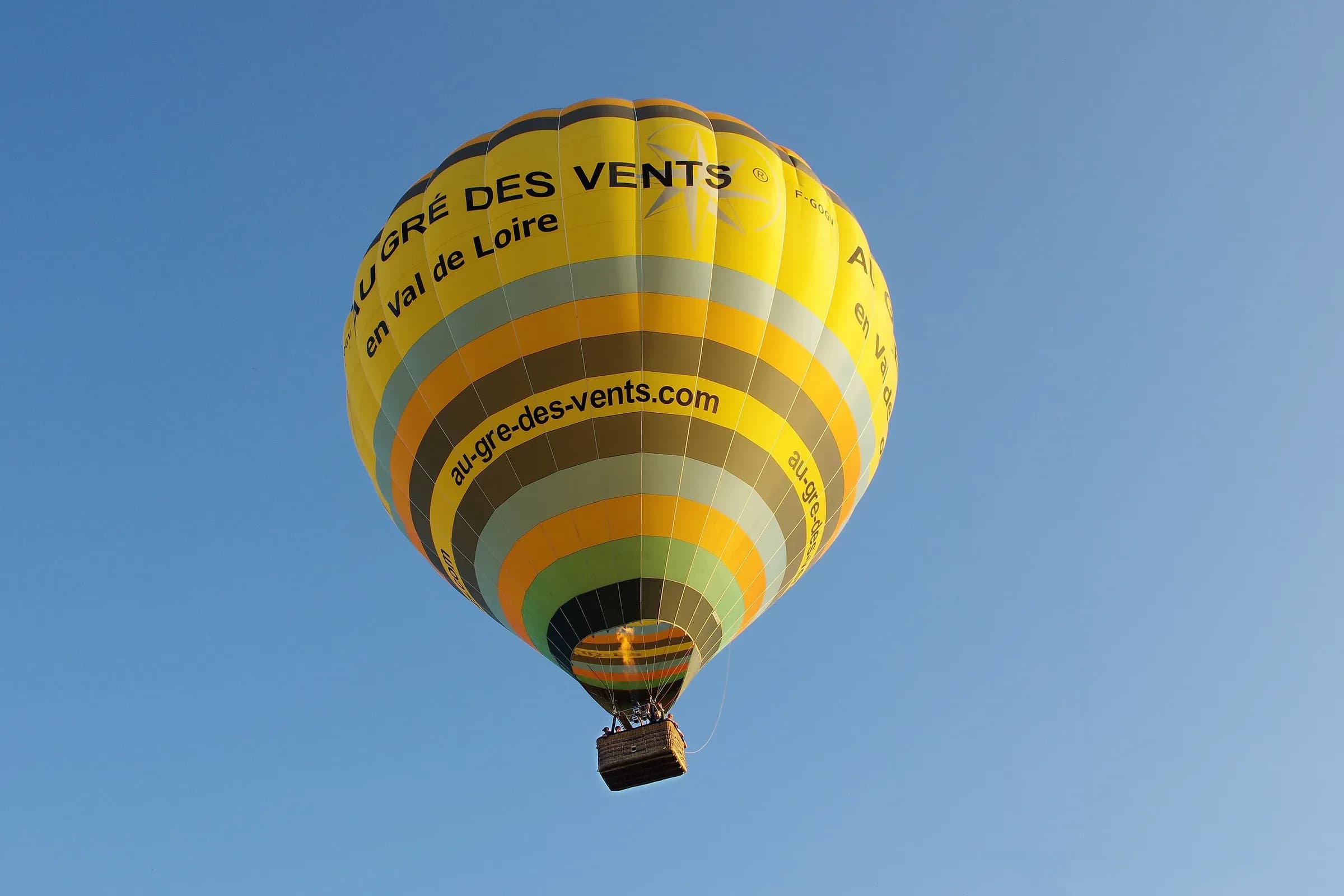 Montgolfière jaune d'Au Gré des Vents en vol dans le ciel bleu de Thésée, dans la vallée du Cher