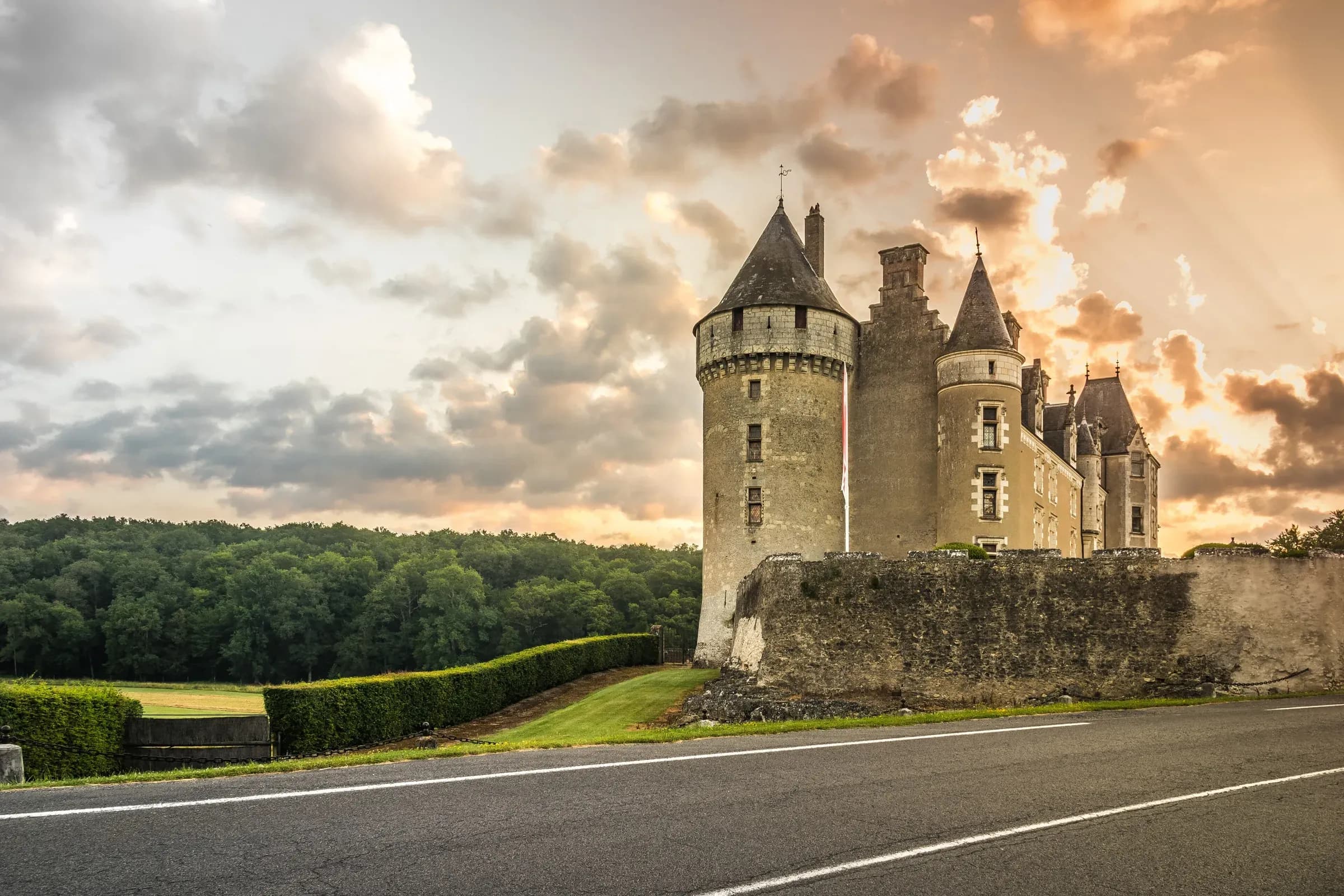 Towers of the Château de Montpoupon above the valley under a sunset sky